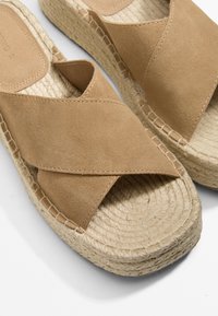 Peščene suede sandale z zaprtimi trakovi in pleteno juto platformo, z teksturiranim zaključkom in šivi ob robovih za večjo vzdržljivost.