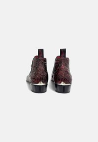 Botines negros y burdeos con patrón floral en relieve, punta redonda y tacón, que presentan un acento plateado en la base y tiradores.