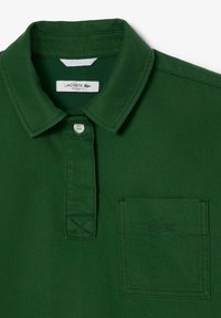 Grünes Lacoste Polo-Shirt mit flachem Kragen, Knopfleiste, einer Brusttasche auf der linken Seite und gesticktem Logo; aus strukturiertem Baumwollstoff gefertigt.