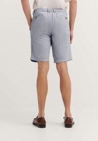 Männer-Shorts mit blauen und weißen Streifen, elastischem Bündchen, zwei Gesäßtaschen und umgeschlagenem Saum. Getragen mit braunen Schuhen.