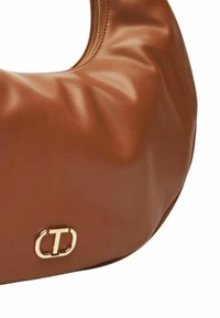 Borsa a tracolla in pelle marrone con un design morbido e gonfio, caratterizzata da una cerniera dorata e un logo circolare in rilievo sulla parte frontale.