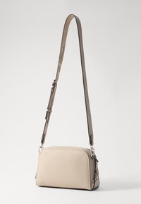 Beige lærveske med en strukturert design, med en lang justerbar stropp og sølvfargede detaljer. Glatt tekstur, kompakt form.