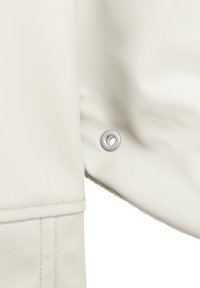 Beżowy materiał ze sztucznej skóry o gładkiej fakturze, z metalowym zatrzaskiem na krawędzi i detalem z podwiniętym obszyciem.