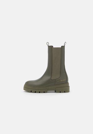 Bottine Chelsea en cuir vert olive avec semelle épaisse, panneaux latéraux élastiques, languettes de tirage et petit logo doré Tommy Hilfiger près du talon.