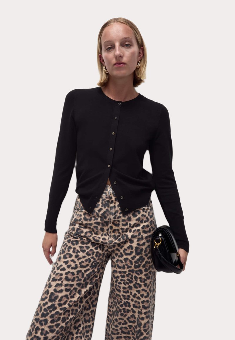 Cardigan noir à boutons, en tissu tricoté, avec des manches longues et un ourlet arrondi, associé à un pantalon à jambes larges à imprimé tigre.