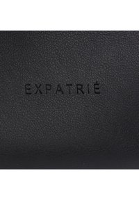 Black textured leather with debossed "EXPATRIÉ" logo. Features a smooth finish and slight grain. Simplistic design, suitable for various settings.