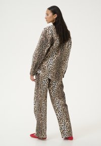 Outfit con stampa leopardata composto da una maglia a maniche lunghe e sviluppo ampio. Presenta uno sfondo beige con macchie marrone scuro.