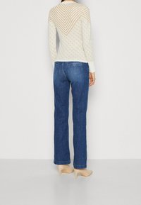 Maglione crema con un motivo a zigzag e maniche lunghe, abbinato a jeans blu a gamba dritta e tacchi alti color nude.