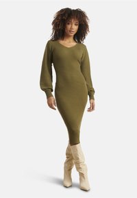 Olive green ribbed knit dress with a V-neck and balloon sleeves, paired with cream slouchy knee-high boots. Form-fitting silhouette.