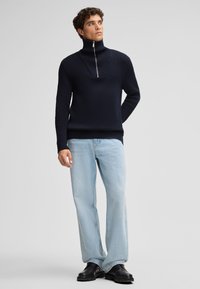 Maglione a coste di colore blu navy con colletto alto e zip a metà, abbinato a jeans a gamba larga di un blu chiaro e stivali chunky neri.