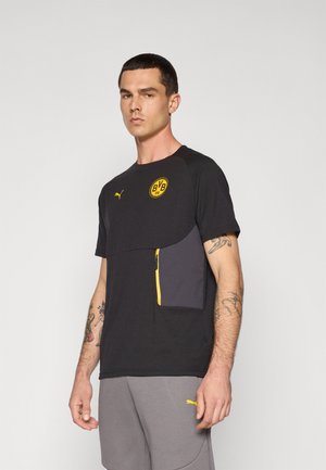 Sort atletisk T-shirt med et gult logo og en lynlåslomme i grå. Korte ærmer og rund hals, lavet af letvægtsmateriale.