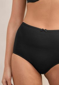 Schwarze Baumwolle hochgeschnittene Slips mit einem dezenten Schleifendetail am Bund und einem gewellten Saum. Weicher Stoff und glatte Verarbeitung.