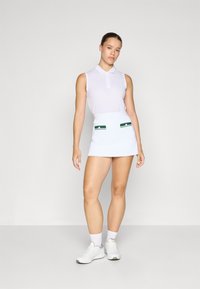 Tricou polo alb fără mâneci, asociat cu o fustă scurtă albă cu accente verzi la buzunare. Țesătură netedă, design ajustat, stil minimalist.