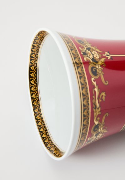 Ceramiczny kubek o czerwonej zewnętrznej powierzchni, zdobiony złotymi kwiatowymi i ozdobnymi wzorami oraz czarno-złotą geometryczną bordiurą przy krawędzi. Wnętrze jest białe.