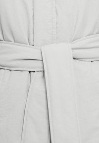 Κοντινή λήψη ενός ανοιχτόχρωμου υφασμάτινου ζωνάρι δεμένου κόμπο γύρω από ένα ένδυμα με ορατή ραφή και υφή.