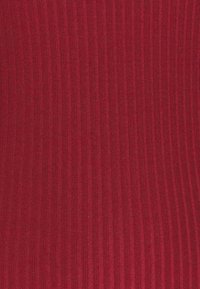 Ribba punainen kangas, jossa on teksturoitu pinta, jossa on pystysuoria viivoja ja pehmeä, joustava ulkonäkö. Materiaali on todennäköisesti neulottu tai venyvä.