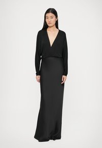 Hosszú fekete ruha, sima anyagból, mély V-nyakkivágással, hosszú ujjakkal és karcsú, testhez simuló sziluettel.