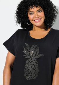Musta t-paita, jossa on hopeinen strassipineapplistus edessä; rento malli, lyhyet hihat ja pyöreä kaula-aukko.