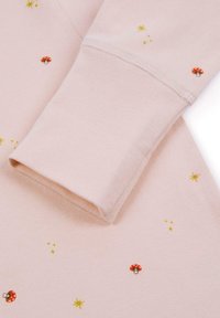 Jasnoróżowy materiał o gładkiej teksturze z rozsianymi wzorami czerwonych grzybów i żółtych gwiazdek. Rękaw jest zawinięty i starannie przeszyty.