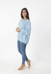 Suéter de punto oversized en azul claro con patrón texturizado, combinado con jeans ajustados en azul oscuro y sandalias de tacón transparente.