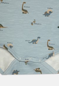 Blå kortermet dress med forskjellige dinosaurprint i jordfarger, med trykknapper nederst, laget av myk bomull.