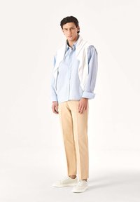 Világoskék csíkos ing, bézs nadrág és fehér tornacipő. Az ing gombos elülső résszel rendelkezik; pulóver van a vállán átdobva; sima anyagtextúra.