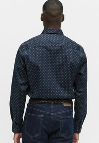 Marinblå skjorta med små, ljusa prickar, knappad krage och långa ärmar. Bärs med mörka jeans och flätad skärp.