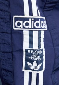 Marinblå Adidas träningsbyxor med vita tre ränder och logopatchar med texten "MÄRKEN MED TRE RANDER".