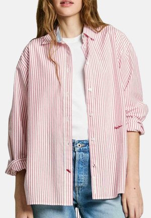 Chemise à rayures rouges et blanches, à manches longues, avec une coupe décontractée, portée avec un t-shirt blanc en dessous et associée à un jean bleu clair.