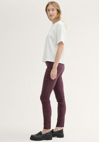 Bijela rebrasta majica kratkih rukava u kombinaciji s bordo slim-fit hlačama i crnim loafericama, prikazana sa strane na svijetloj pozadini.