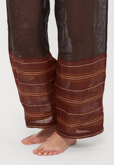 Pruunid, läbipaistvast kangast püksid laia, elastse vöökohaga ja triibuliste aktsentidega oranži ja kullakarva toonides ääres. Pehme tekstuur, lõdvestunud lõige.