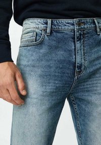 Světle modré džíny vyrobené z denimu s klasickým pětioktovým designem, jemným blednutím a kovovým zapínáním na knoflík. Texturovaná látka s jemným povrchem.
