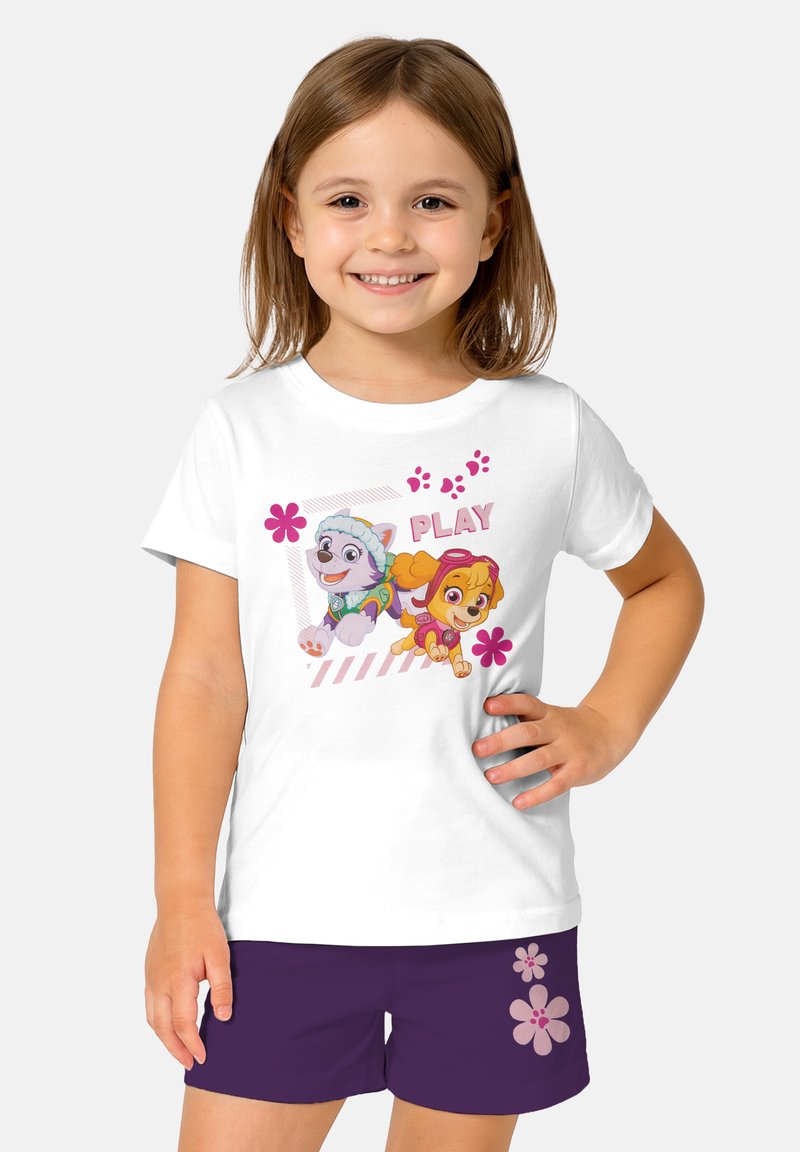 Maglietta bianca con vivaci disegni di cartoni animati di due cani, con la parola "GIOCA" e accenti floreali rosa. Abbinata a pantaloni corti viola scuro.