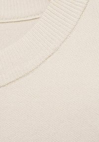 Gros plan sur un tissu tricoté beige montrant un col en V côtelé et la surface texturée d'un pull doux.