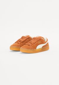 Suede sneakers i oransje med hvit sidestripe, rund tå, tykk gummisål og flate snørebånd. Merking på tungen og siden. Casual design.