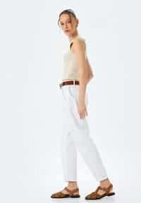Top beige senza maniche, pantaloni bianchi su misura e sandali marroni con cinturini. Tessuto morbido con un design aderente e una leggera texture.