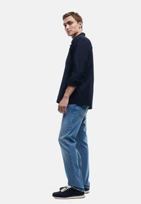 Marineblauwe, lange mouwen shirt met opgerolde manchetten, gecombineerd met lichtblauwe spijkerbroeken. Zwarte sneakers met witte veters. Eenvoudig en casual ontwerp.