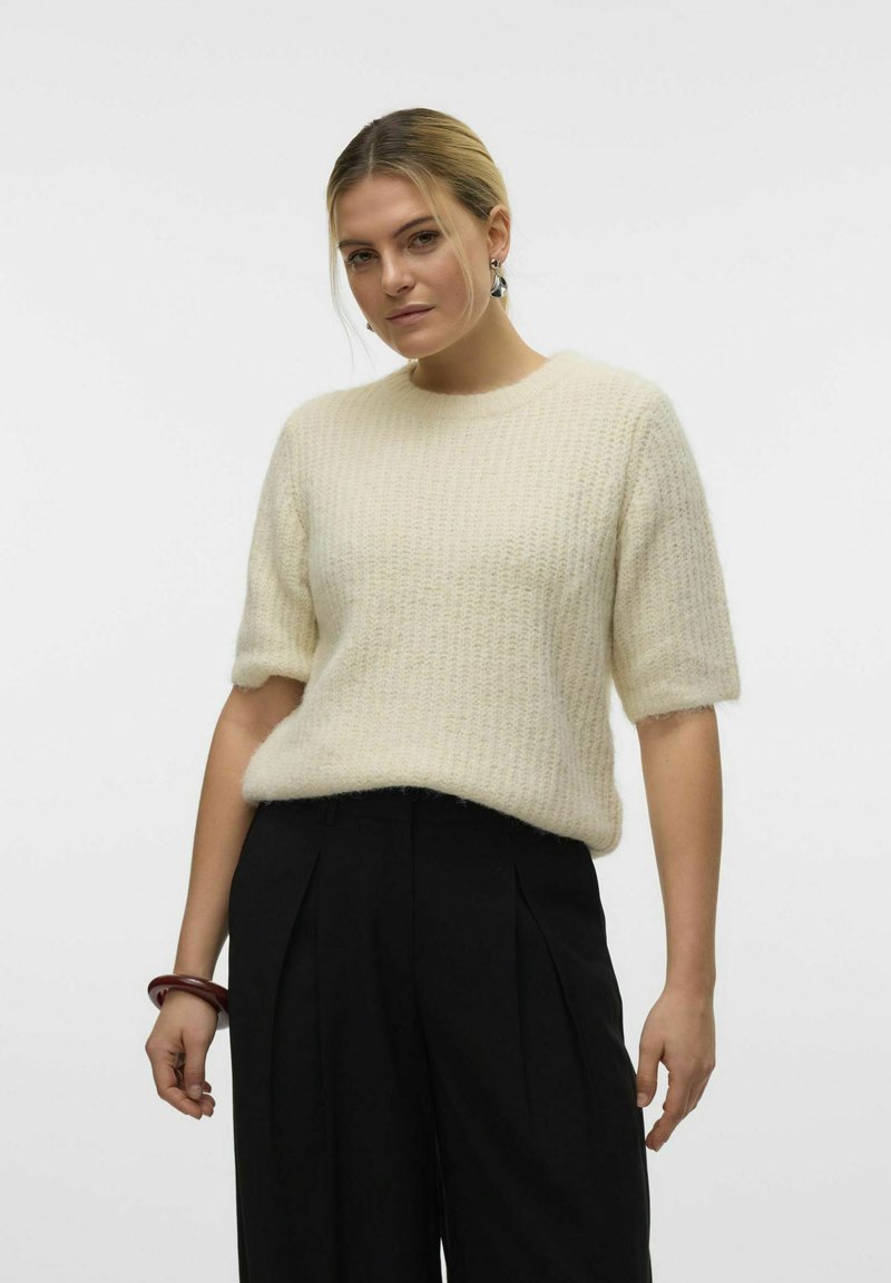Luffende cremede sweater med rund halsudskæring og korte ærmer, kombineret med høj-taljede sorte bukser. Tekstureret strikket stof.