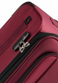 Burgundy soft-sided suitcase corner showing dual zipper locks secured with a TSA-approved combination lock.