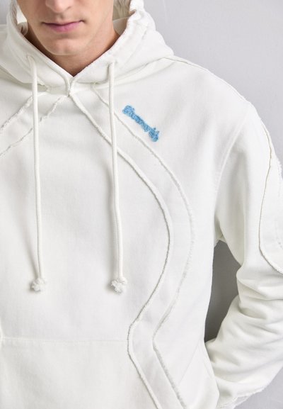 Sudadera blanca con costuras texturizadas y un logo bordado azul. Cuenta con un bolsillo tipo canguro y capucha con cordón ajustable.