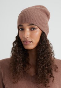 Beanie lavorato a maglia in morbida lana marrone con una trama a coste. Il design presenta una forma morbida e senza hardware o accenti visibili.