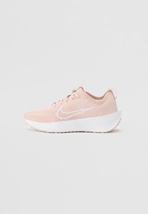 Gaiši rozā sporta apavi ar elpojošu sietu augšdaļu, baltu Nike zīmolu un biezu balto zoli. Satur detalizētu šuvumu un šņorēšanu.