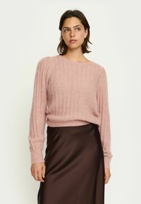Roze gebreide trui met ribbelstructuur, wijde halslijn en lange mouwen, gecombineerd met een bruine satijnen rok.