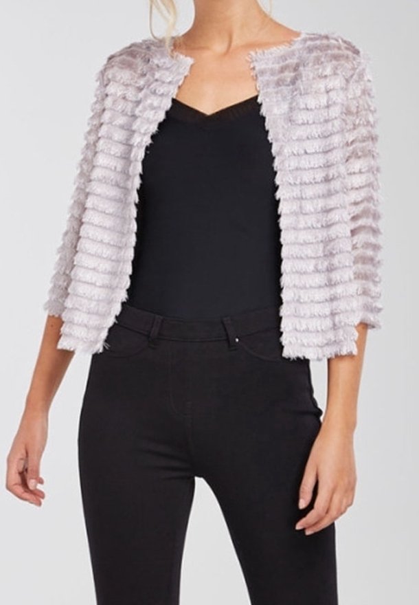 Chaqueta de piel sintética en gris claro con un patrón texturizado y acanalado; diseño abierto al frente y mangas tres cuartos. Combinada con una camiseta negra y pantalones.