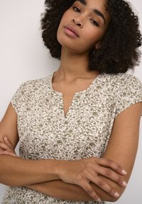 Robe à motif floral en blanc et vert olive. Dotée d'un décolleté en V et de manches courtes, fabriquée en tissu doux avec une finition légèrement texturée.