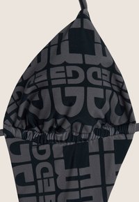 Musta bikiniyläosa, jossa toistuva tummanharmaa geometrinen kuvio. Materiaali on sileää, ja siinä on poimuttu sauma helman kohdalla.