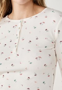 Top a maniche lunghe color crema con un'apposita patta con bottoni, decorato con un motivo di piccoli funghi e foglie in tonalità terrose.