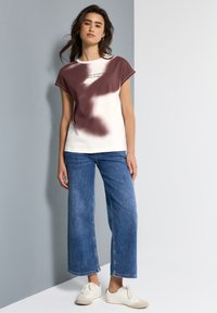 Hvid t-shirt med maroon pletter og tekst, parret med lyseblå vidde jeans og hvide sneakers. Enkelt design og løs pasform.