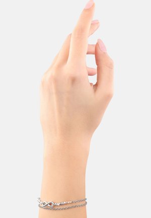 Zilveren oneindigheid charme armband met gestructureerde ketting en kleine kralen, gedragen aan een hand met een natuurlijke manicure tegen een effen achtergrond.
