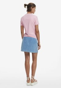 Pink short-sleeve t-shirt paired with a light blue denim skirt, featuring a simple cut and minimal design. Model wears white strappy sandals.